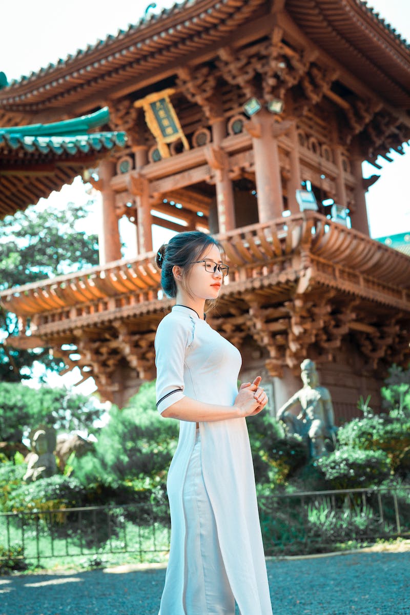 Pretty young Asian woman standing against old temple on sunny weather