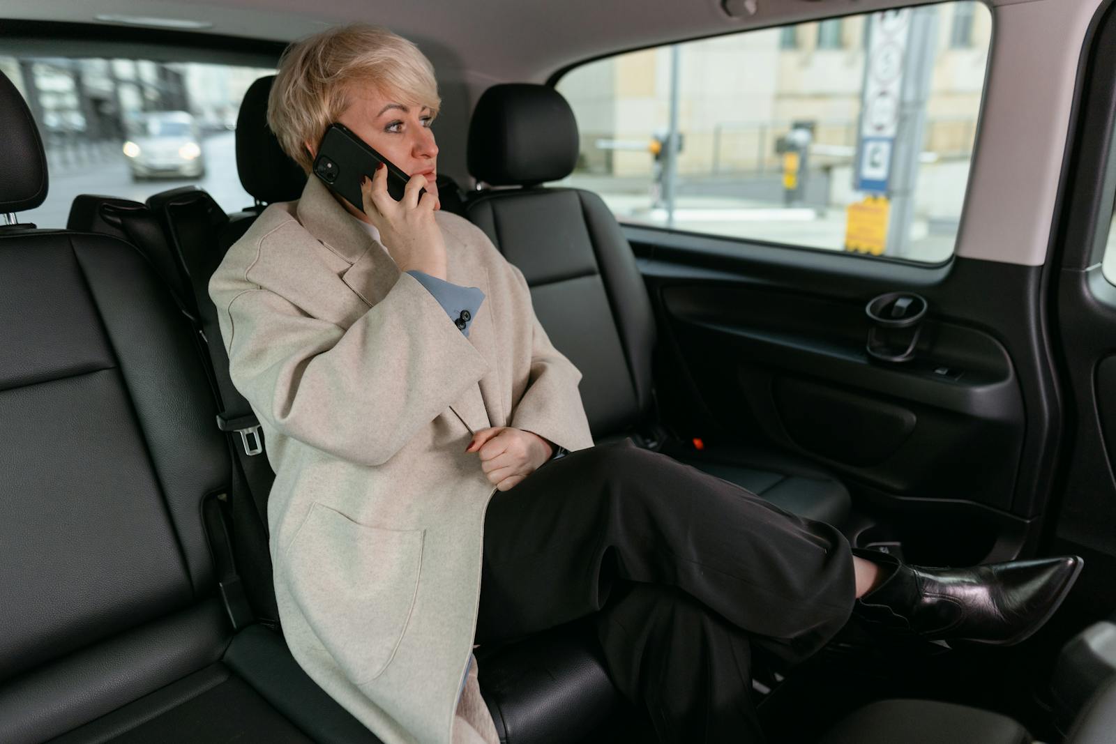 Woman in Brown Coat Sitting inside the Car while Having a Phone Call